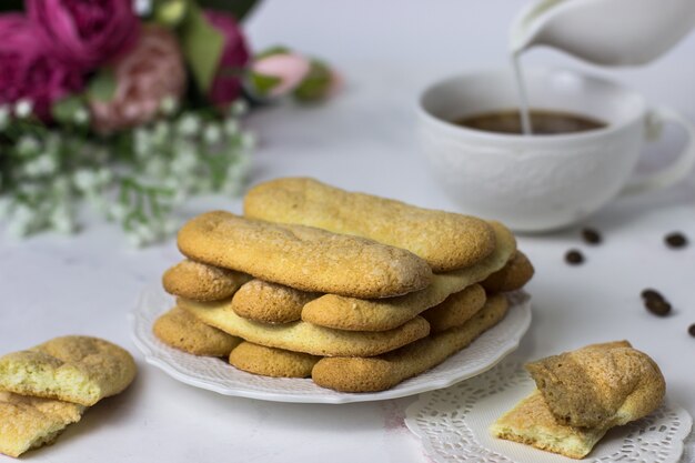 Biscuits biscuits savoyardi, café et fleurs sur une surface en marbre blanc