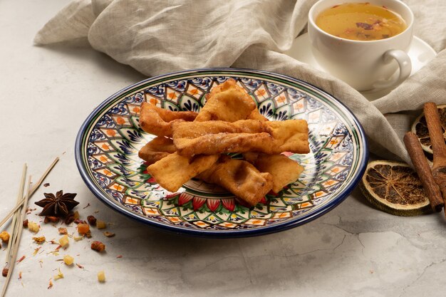 Biscuits de broussailles fraîchement cuits au four avec du sucre en poudre dans une assiette en céramique ouzbek nationale décorative avec un motif traditionnel. Pâtisseries sucrées pour le dessert pour le thé