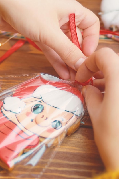 Biscuits de cadeaux de Noël avec glaçage coloré sur table en bois Les mains des femmes attachent un ruban rouge sur le sac de gin...