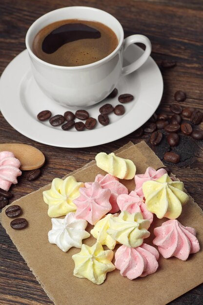 Biscuits colorés de meringue et tasse de café sur la table en bois foncée