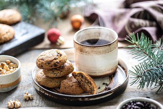 Biscuits faits maison avec des noix et du café dans une tasse en céramique sur une table en bois avec des jouets et des branches d'arbres de Noël.