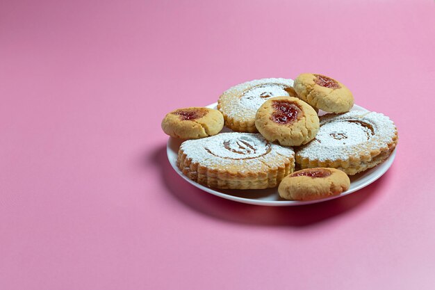 Biscuits faits maison sur une plaque blanche sur fond rose Confiture et sucre en poudre