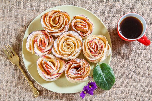 Biscuits faits maison avec des pommes en forme de rose sur une assiette et une tasse de café sur un sac. Vue de dessus