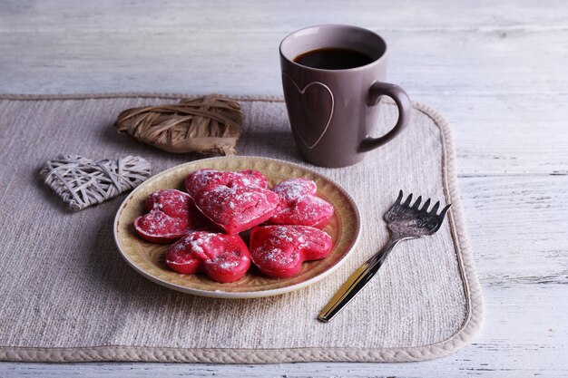 Biscuits en forme de coeur sur une assiette avec une tasse de café sur une serviette et un fond de planches de bois de couleur