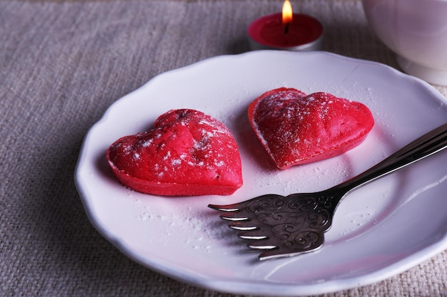Biscuits en forme de coeur dans une assiette avec une tasse de café et des bougies sur une serviette, sur fond de planches de bois rustique
