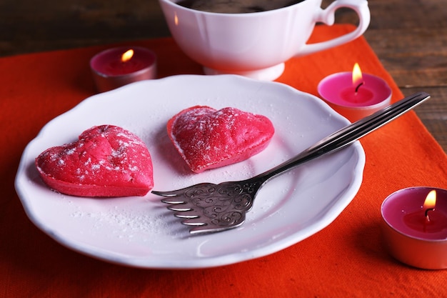 Biscuits en forme de coeur dans une assiette avec une tasse de café et des bougies sur une serviette, sur fond de planches de bois rustiques