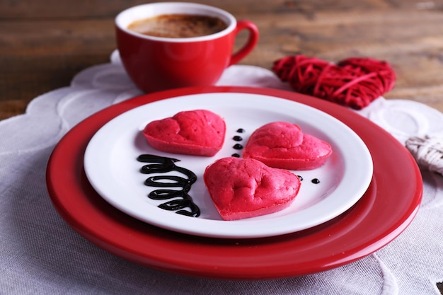 Biscuits en forme de coeur dans une assiette avec une tasse de café sur une serviette, sur fond de planches de bois rustique