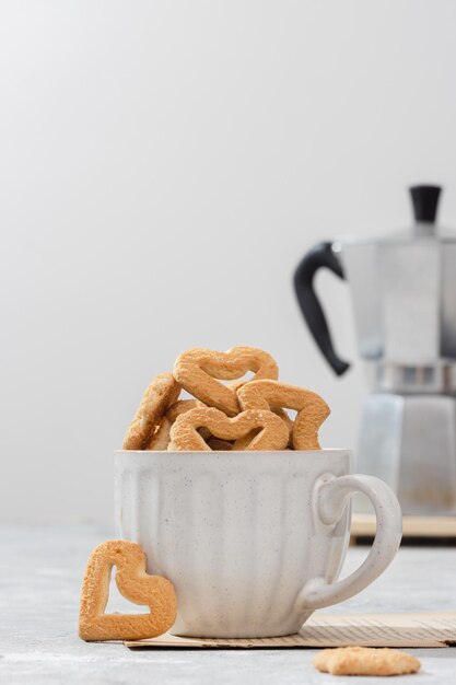 Photo biscuits en forme de coeur dans une tasse blanche fond clair avec une cafetière