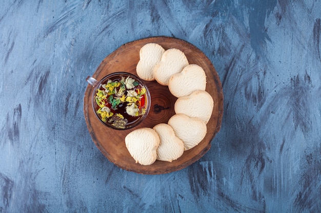 Biscuits en forme de coeur frais parfumés et tasse de tisane sur morceau de bois.