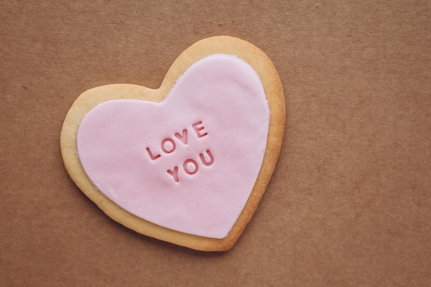 Biscuits en forme de coeur avec glaçage rose et l'inscription love you située sur un fond de papier kraft avec un espace pour vos cadeaux textxALvalentine's Day