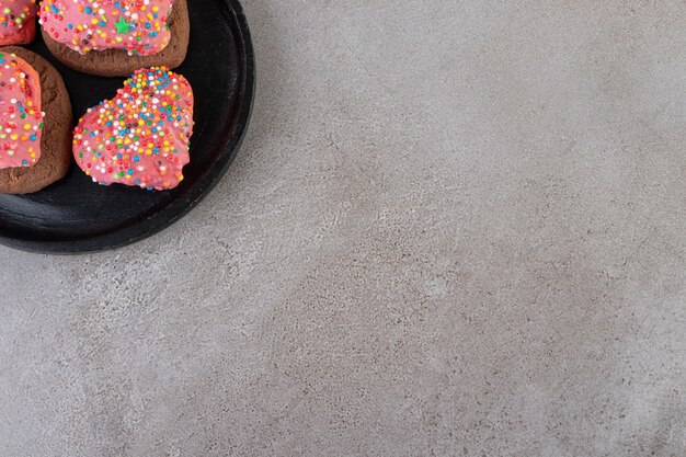 Biscuits en forme de coeur avec des paillettes placées sur une plaque noire.