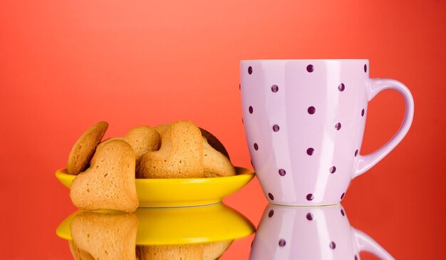 Biscuits en forme de coeur sur plaque jaune et tasse sur fond rouge