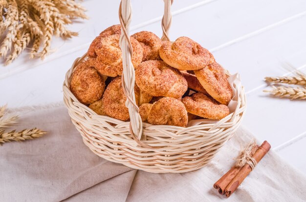 Biscuits frais et savoureux à la cannelle dans un panier en osier sur fond de bois blanc