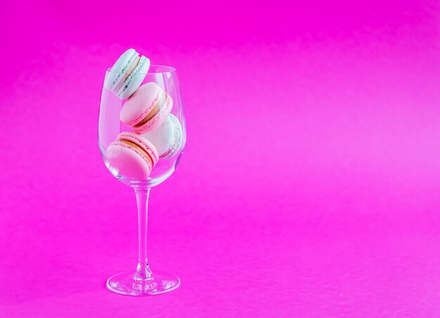 Biscuits français macarons dans un gobelet en verre sur un fond rose.