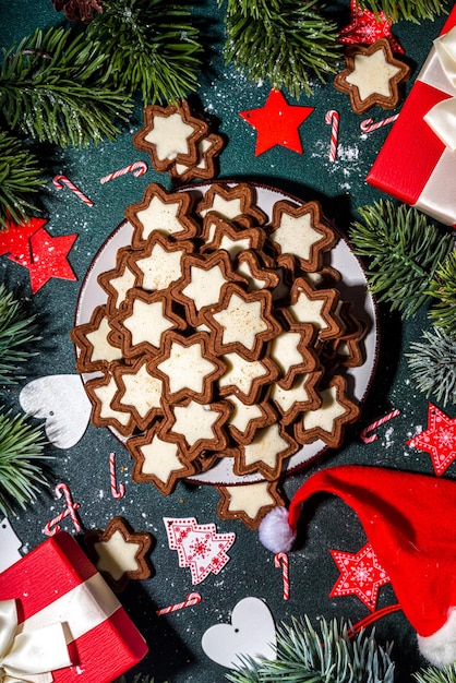 Les biscuits glacés à l'étoile de Noël, le chocolat noir et blanc traditionnel, les biscuits au pain d'épice avec des cadeaux de décoration de vacances, la branche de l'arbre de Noël sur la table vert foncé, la vue supérieure de l'espace de copie