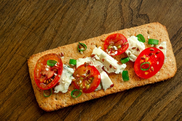 Biscuits à grains entiers pain croustillant fin avec tomates au fromage oignon vert et graines de lin sur fond de bois naturel