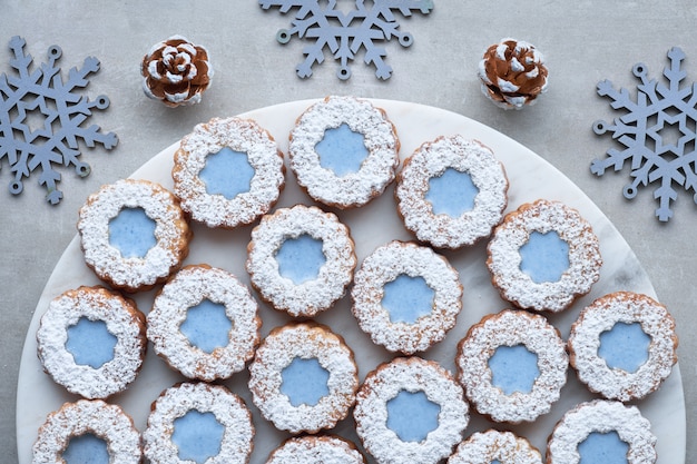 Biscuits Linzer à fleurs blanches et bleues sur une surface en pierre claire avec des décorations d'hiver