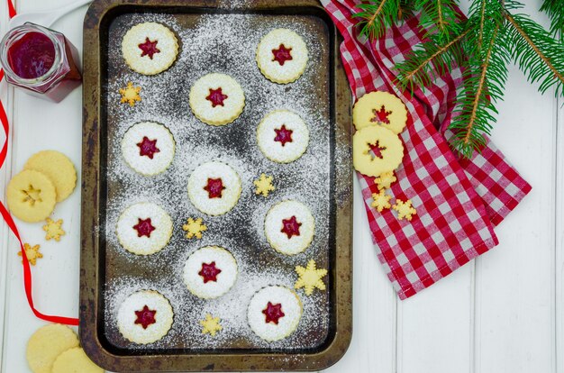 Biscuits Linzer de Noël faits maison remplis de confiture de fraises sur une plaque à pâtisserie sur un bois blanc