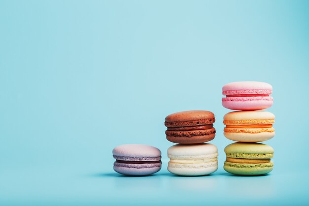 Les biscuits macaroni de différentes couleurs sont disposés en forme d'étapes pyramidales sur fond bleu.