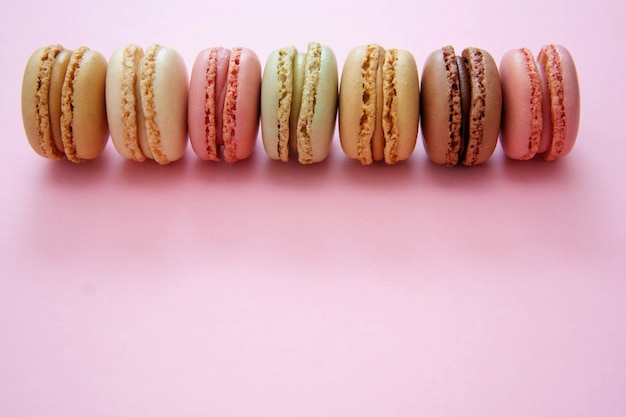 Biscuits macarons français traditionnels colorés, sur table rose avec espace de copie.