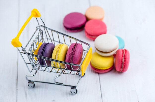 Les biscuits macarons se trouvent dans un panier pour enfants pour faire du shopping sur le fond de bois blanc