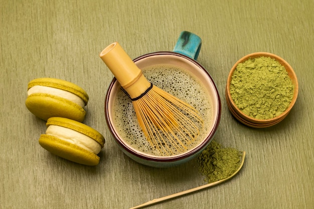 Des biscuits de macaroon vert, du fouet de bambou dans une tasse avec du thé matcha.