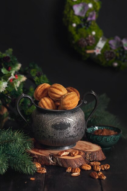 Biscuits maison traditionnelle russe Noix - Oreshki avec du lait concentré sur un pot vintage sur un support en bois entouré de branches d'épinette et de noix éparpillées.