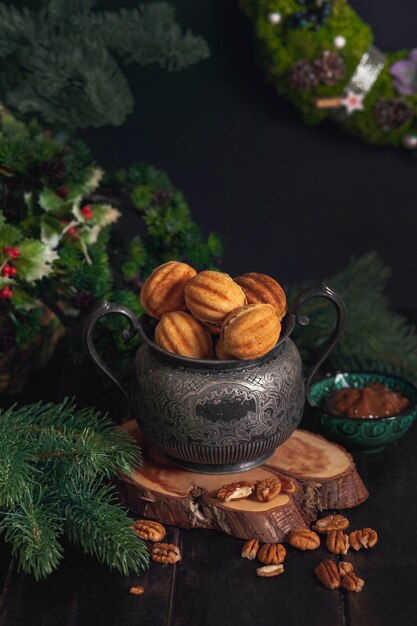 Biscuits maison traditionnelle russe Noix - Oreshki avec du lait concentré sur un pot vintage sur un support en bois entouré de branches d'épinette et de noix éparpillées.