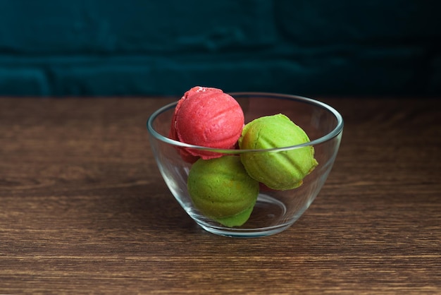 Biscuits multicolores sous forme de noix avec crème fourrée dans un vase en verre transparent sur table sur fond sombre