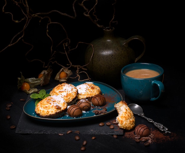 biscuits à la noix de coco avec du chocolat sur un plat bleu-vert foncé avec une tasse de café sur fond noir