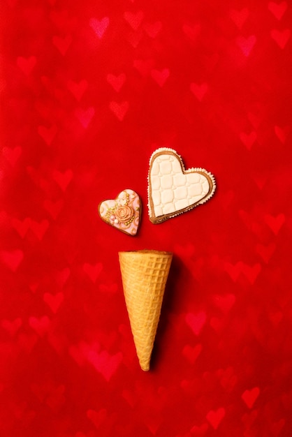 Biscuits de pain d'épice avec glaçage coeurs en cornet gaufré sur fond rouge. Notion de Saint Valentin. Mise à plat. vue de dessus