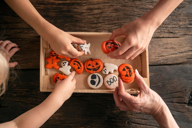 Biscuits de pain d'épice d'Halloween dans une boîte sur une table en bois Les mains prennent des cookies Biscuits au gingembre drôles pour Halloween sur la table