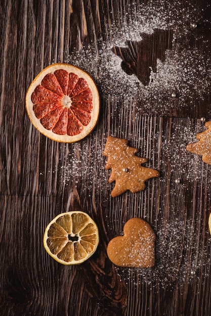 Biscuits de pain d'épice en sapin de Noël et en forme de cœur, sucre en poudre sur table en bois, agrumes, vue de dessus