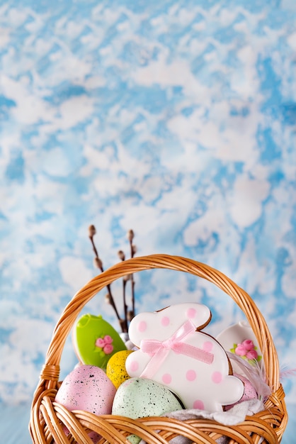 Biscuits de Pâques, lapins et oeufs de Pâques multicolores dans un panier sur fond bleu clair