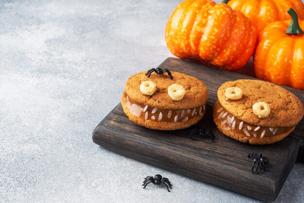 Biscuits à la pâte de crème en forme de monstres pour la fête d'Halloween. Visages faits maison drôles faits de biscuits à l'avoine et de lait concentré bouilli. espace de copie