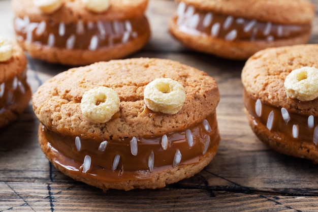 Biscuits à la pâte de crème en forme de monstres pour la fête d'Halloween. Visages faits maison drôles faits de biscuits à l'avoine et de lait concentré bouilli.