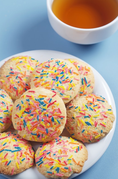 Biscuits avec des pépites colorées dans une assiette et une tasse de thé sur une table bleue se bouchent