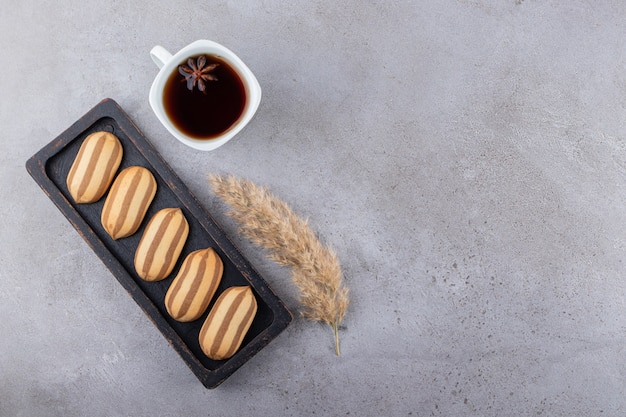 Biscuits à rayures en planche de bois sombre avec une tasse de thé.