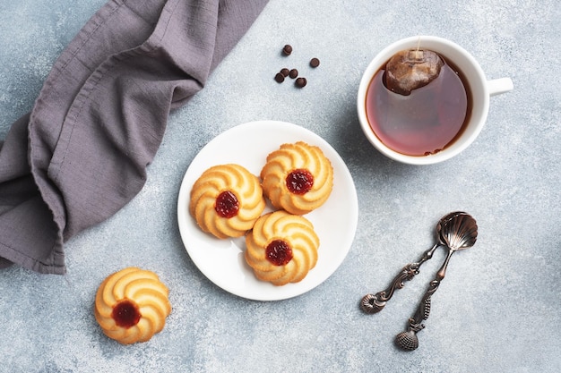 Biscuits sablés Kurabye avec confiture de baies dans une assiette et une tasse de thé. Délicieux dessert, fond de béton gris avec espace de copie.