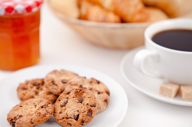 Biscuits et une tasse de café sur des assiettes blanches avec des croissants de sucre et du lait et un pot de confiture