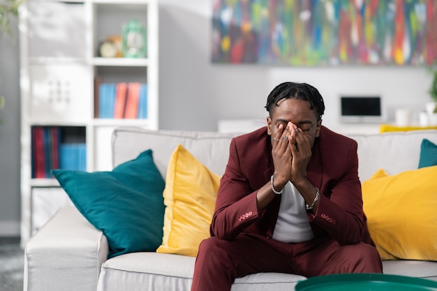 Bisnessman triste désemparé vêtu d'un costume est assis sur un canapé dans le bureau couvre le visage avec les mains