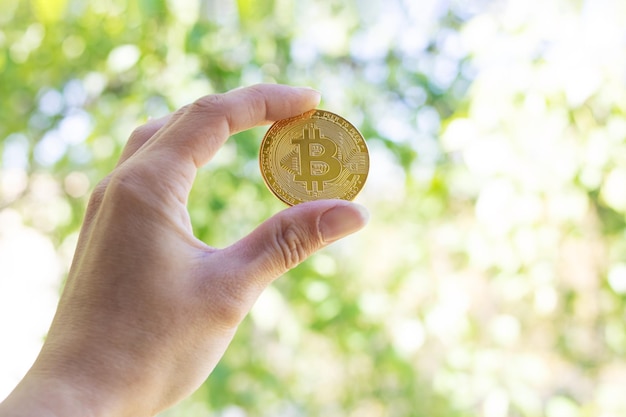 Bitcoin à la main sur fond de verdure au soleil