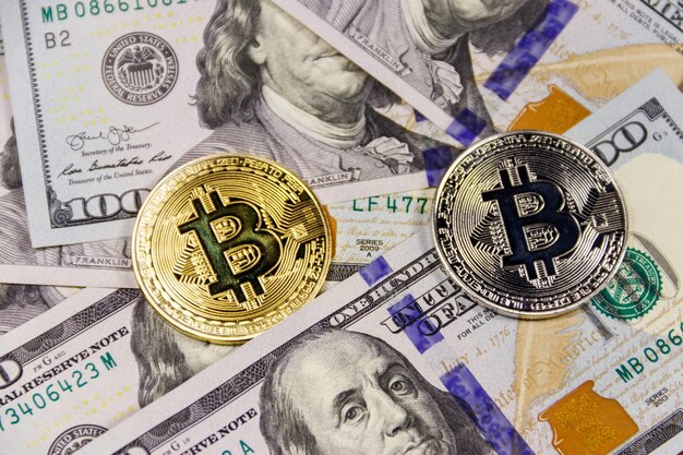 Bitcoins d'or et d'argent sur fond de billets de cent dollars