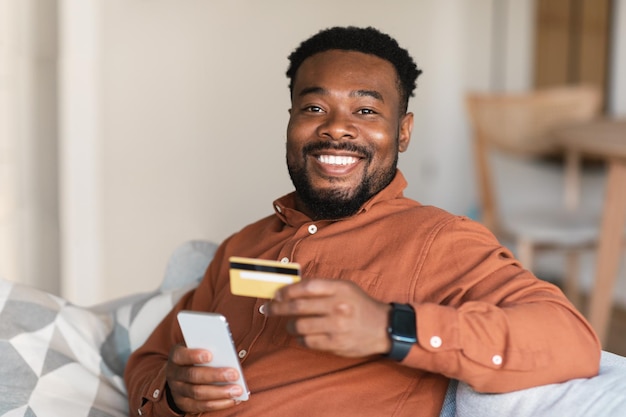 Black Guy Shopping en ligne en utilisant le téléphone et la carte de crédit à l'intérieur