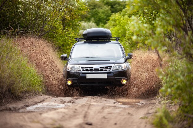 Black Subaru Forester se déplaçant sur une route forestière sale faisant beaucoup d'éclaboussures d'eau