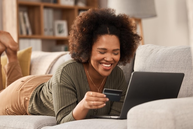 Photo black woman credit card and laptop on sofa for online shopping digital payment and fintech account happy female person computer banking and money for sales password and ecommerce finance at home