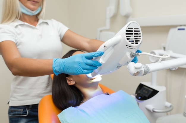 Blanchiment dentaire par UV dentaire, assistant dentaire prenant soin du patient, yeux protégés par des lunettes.