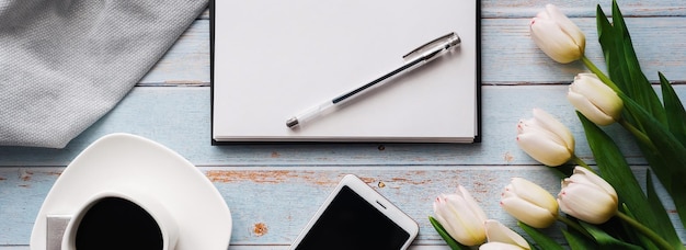 Blancs de printemps du lieu de travail d'un pigiste avec un bouquet de tulipes blanches un smartphone un bouquet blanc vide et une tasse de café dans ses mains sur fond de bois