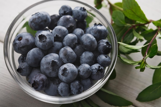 Bleuets biologiques frais dans un bol en verre agrandi. Tas de myrtilles mûres et de menthe sur une table en bois rustique, vue de dessus