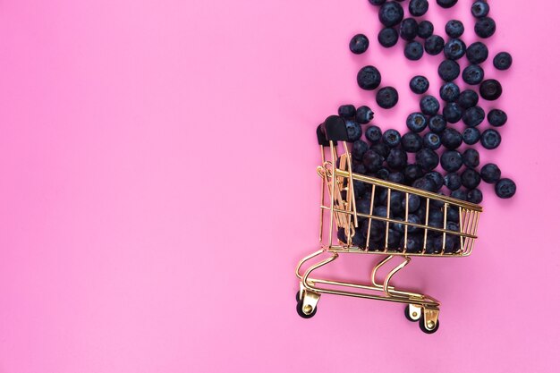 Bleuets dans un chariot d'épicerie sur fond rose. Bleuets épars près d'un chariot d'épicerie sur fond rose.